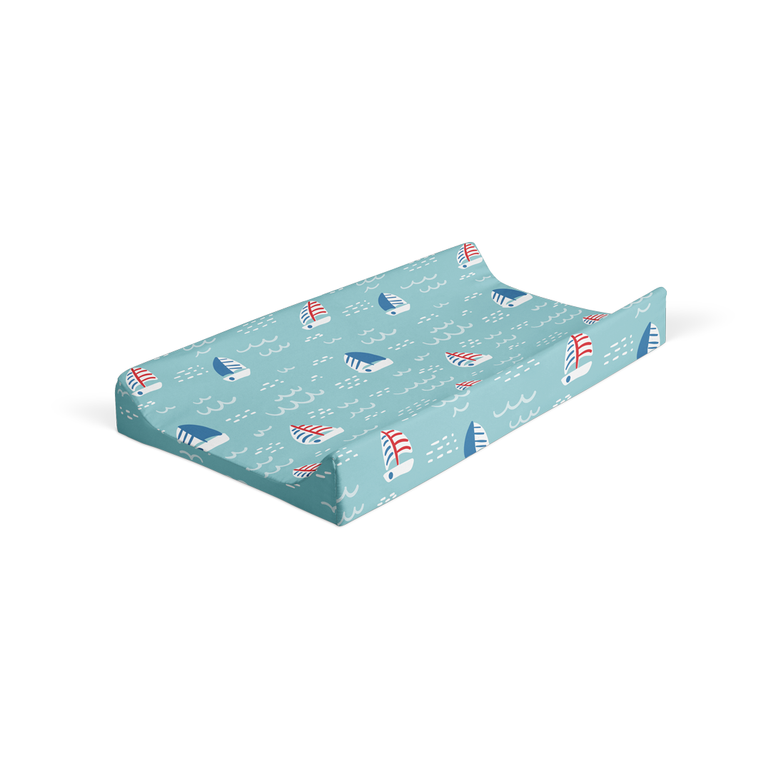 Angled view changing pad cover with sailboat pattern on blue ocean doodle background.